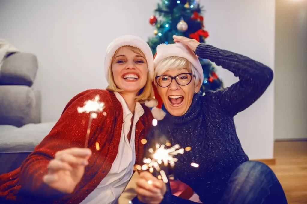 Two joyful people holding sparklers in front of a Christmas tree.