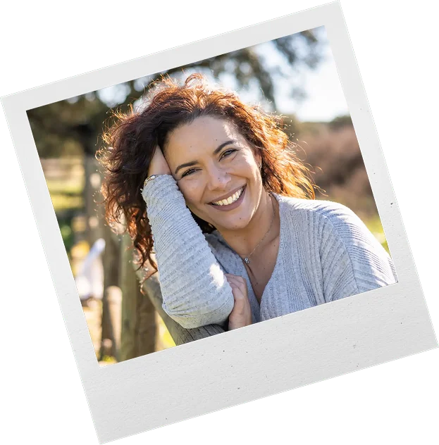Smiling woman with curly hair outdoors on a sunny day.