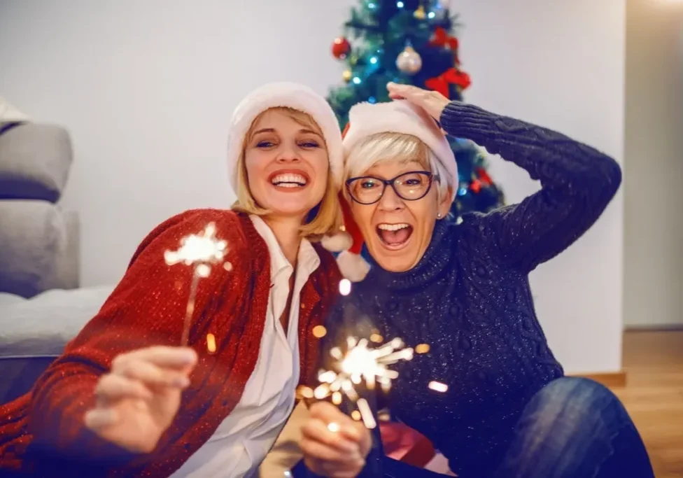 Two joyful people holding sparklers in front of a Christmas tree.